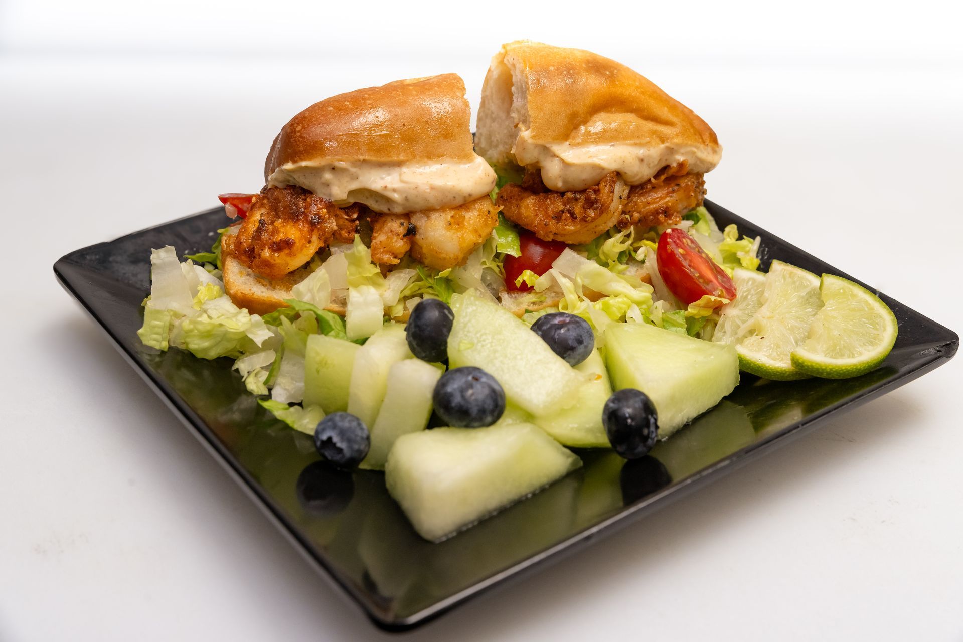 Plate of burgers with fries and cucumber salad, garnished with blueberries and lime wedges