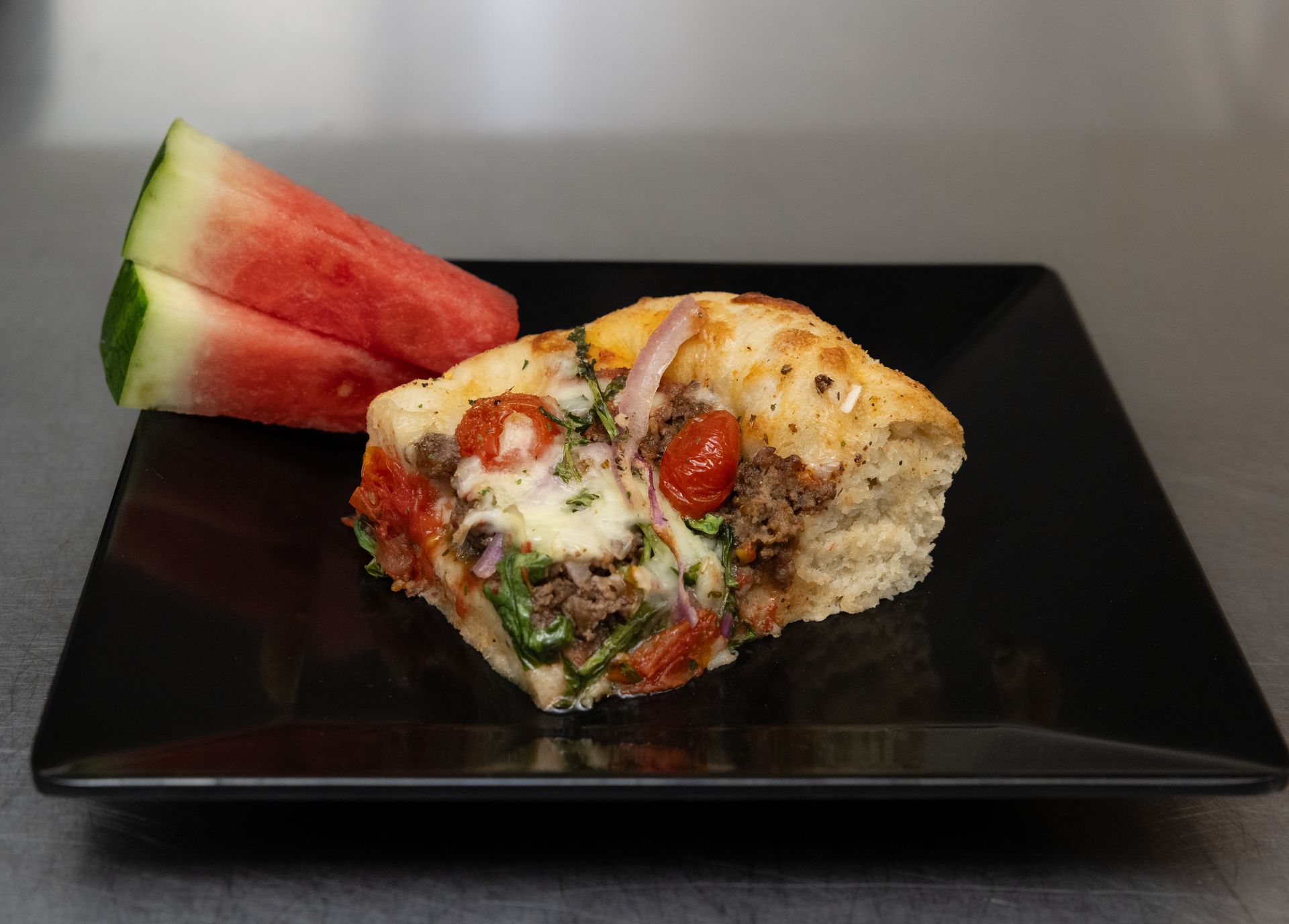 Watermelon wedge and a slice of savory pie on a black plate
