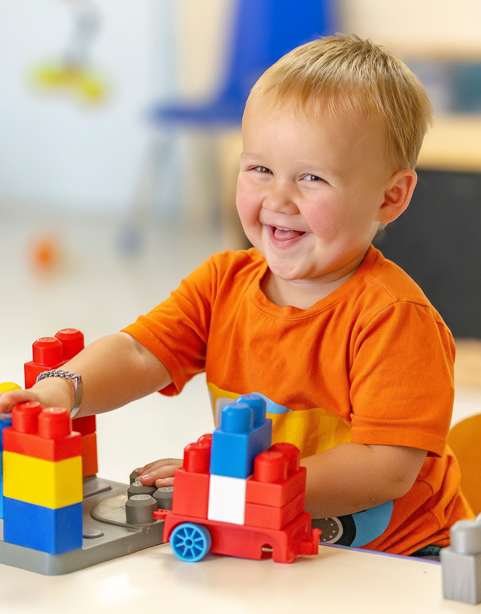 Smiling child in orange shirt building with colorful blocks at a table