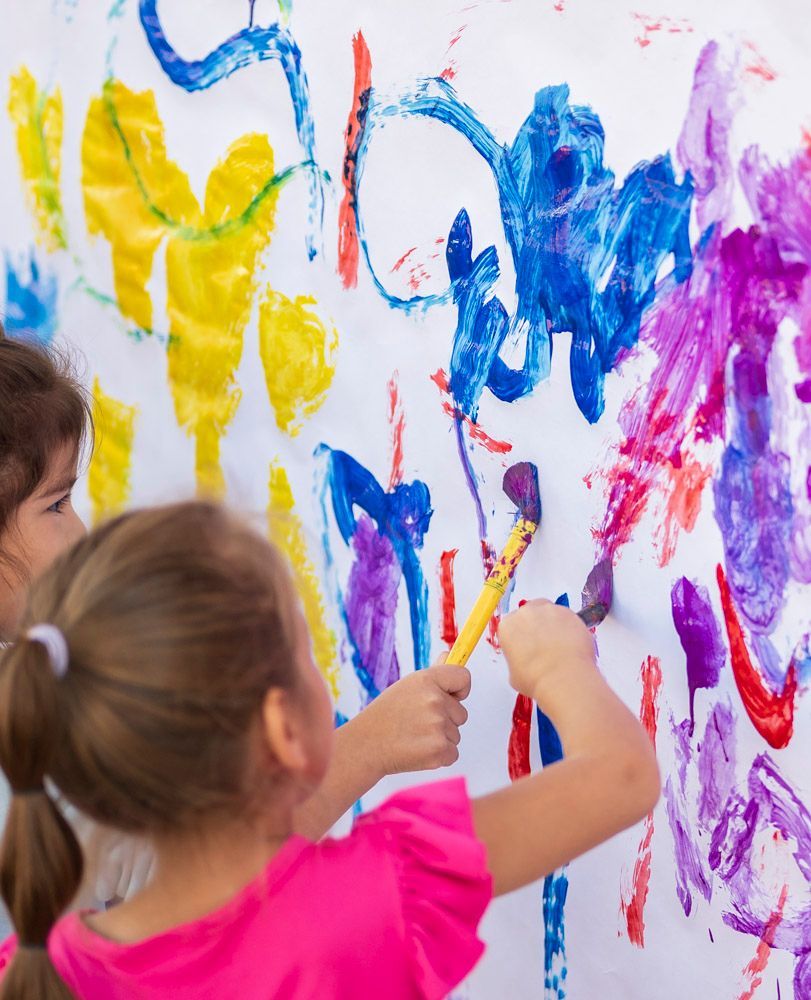 Children painting colorful brushstrokes on a white wall or canvas