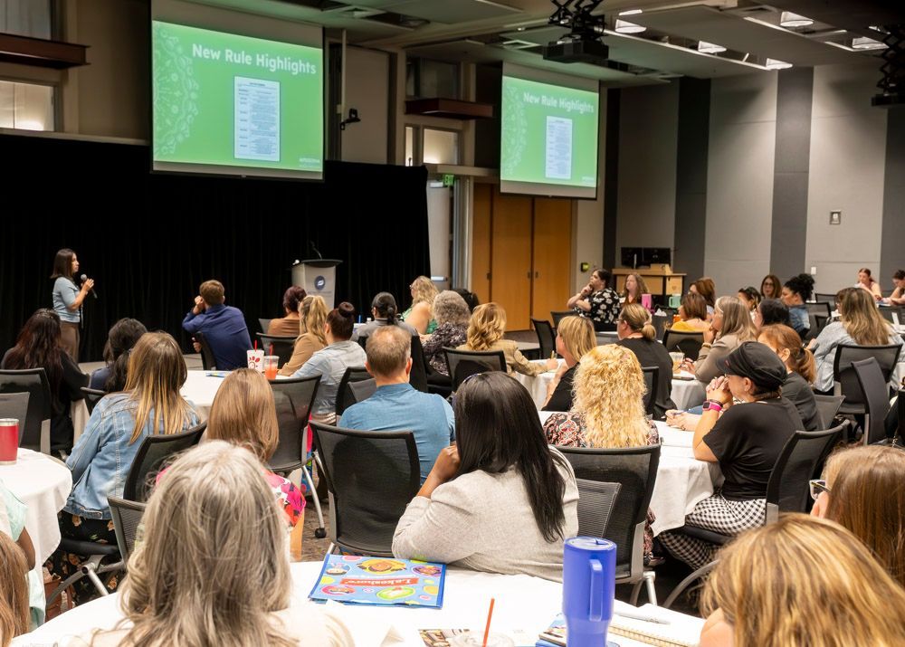 Conference audience facing two green presentation slides in a large meeting room