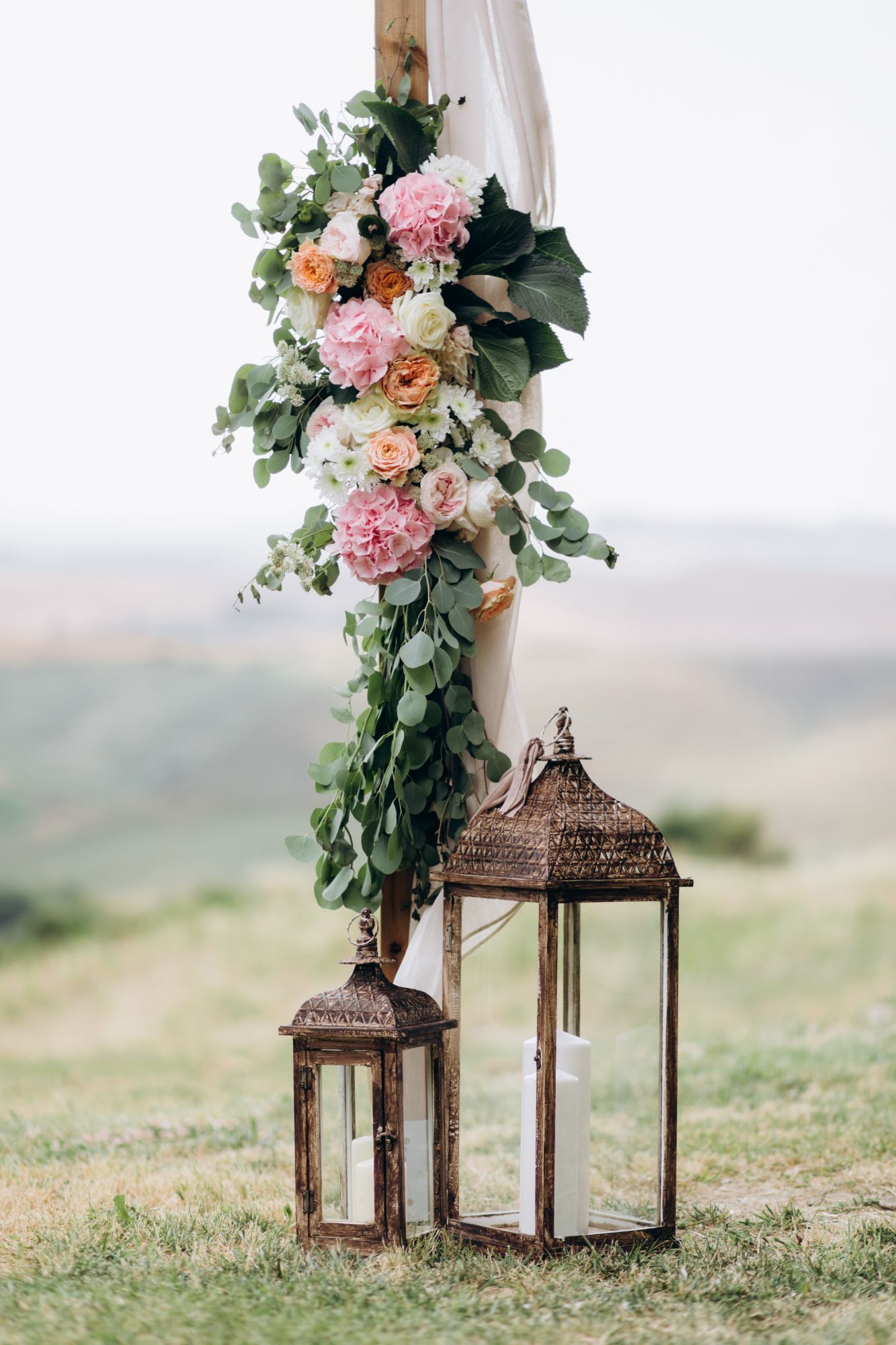 A wooden arch decorated with flowers and lanterns in a field.