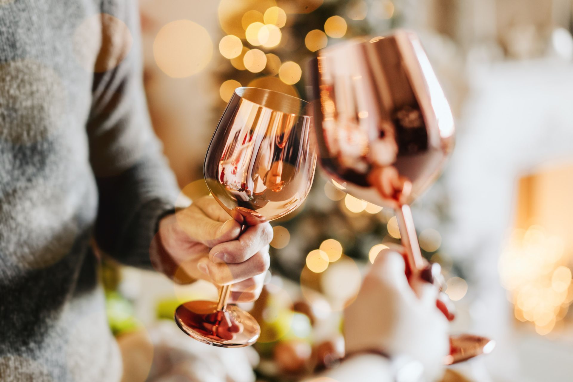 A person is holding two wine glasses in front of a christmas tree.