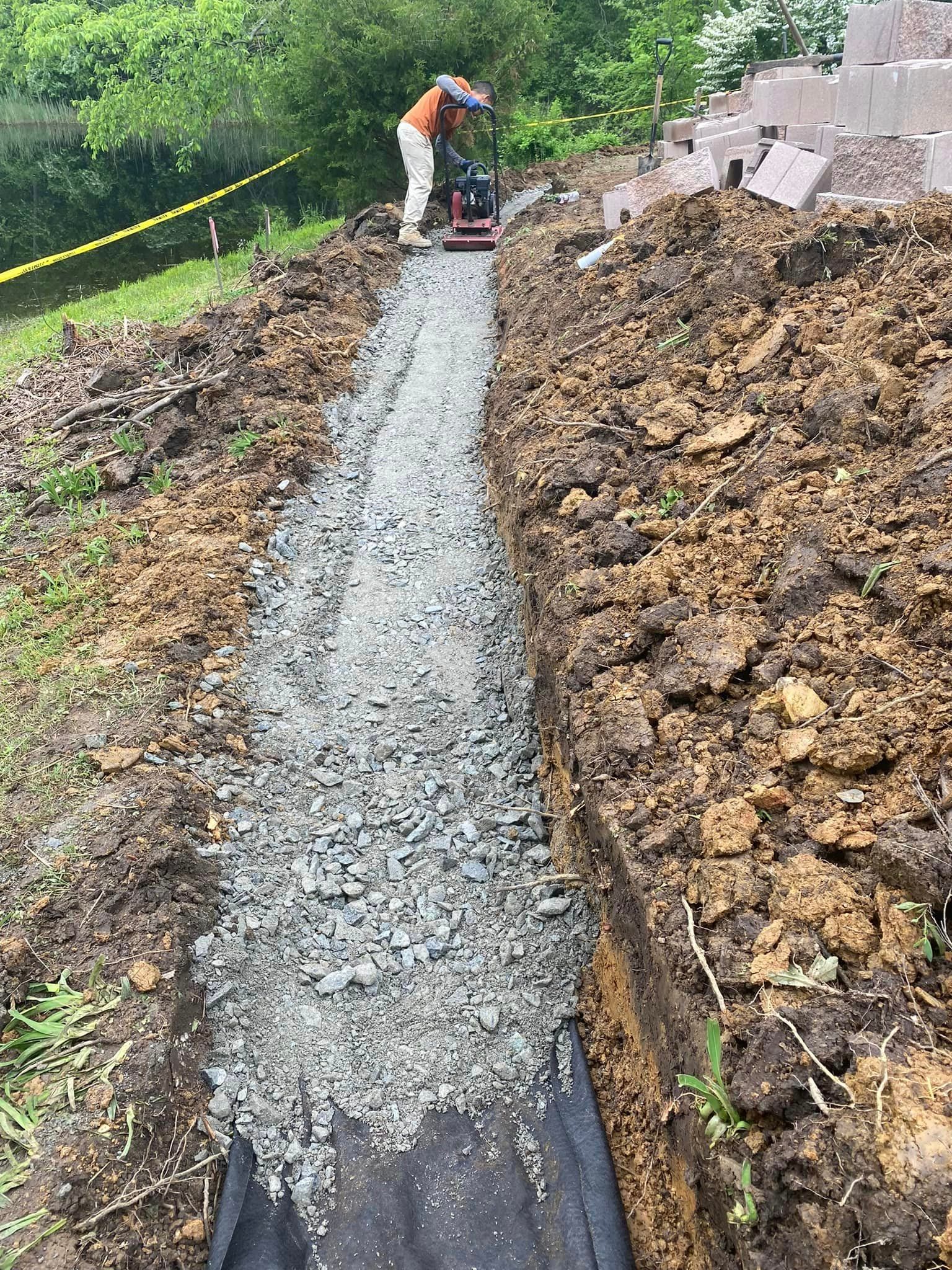 Man is laying gravel in a trench in the dirt.