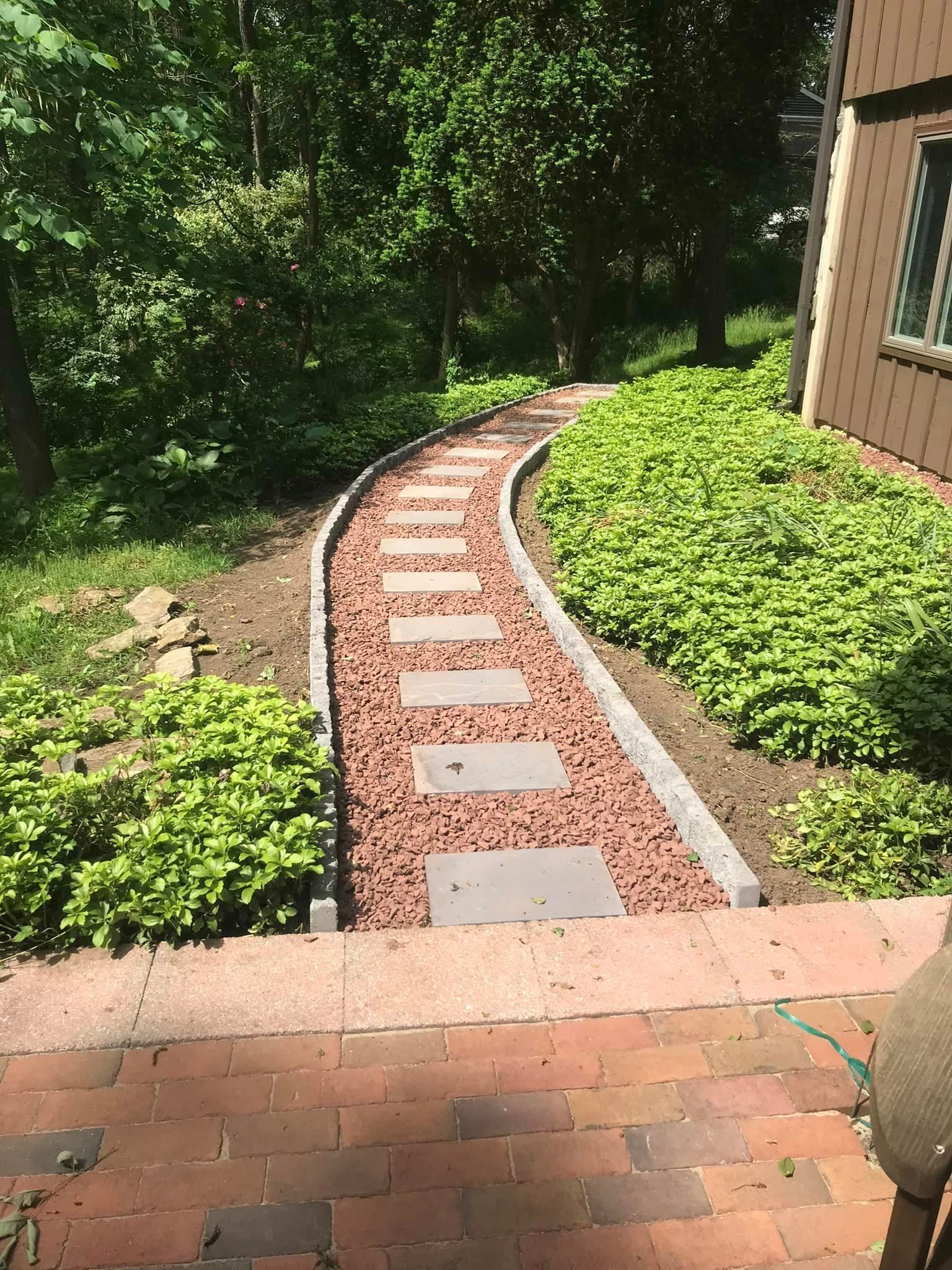 A brick walkway leading to a house surrounded by trees and bushes.