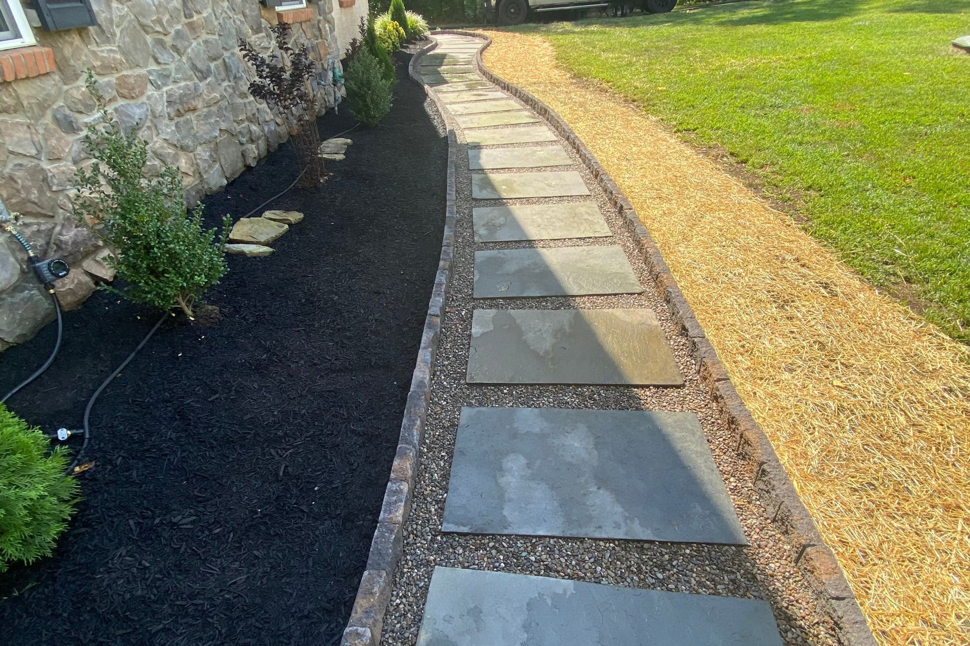 A walkway leading to a house with a stone wall and gravel.