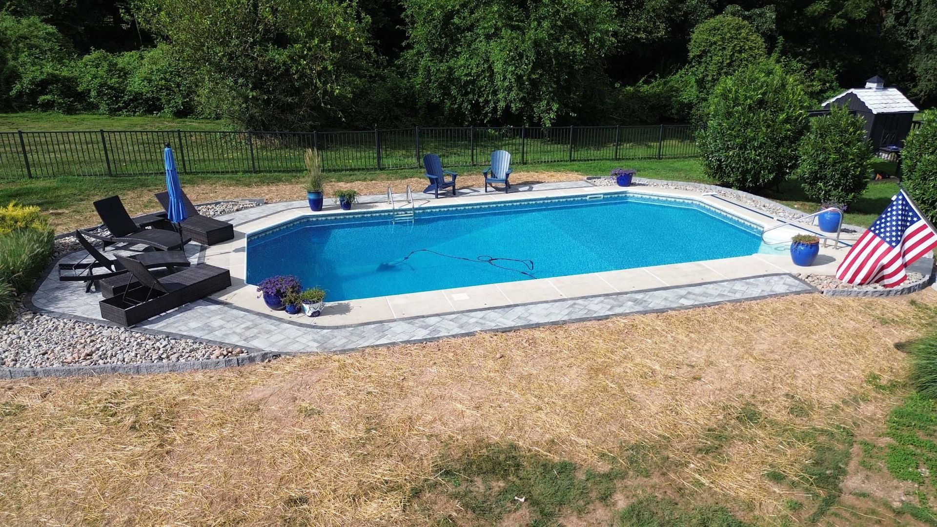 A large swimming pool surrounded by chairs and umbrellas in a backyard.