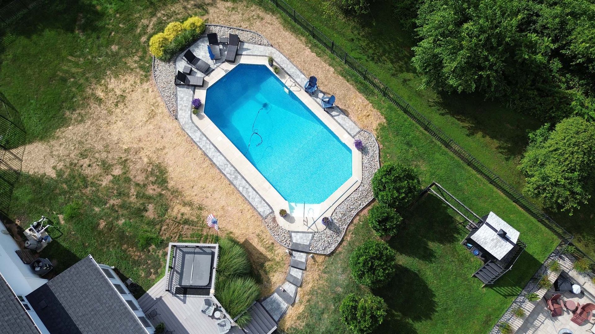 An aerial view of a large swimming pool in a backyard surrounded by trees.