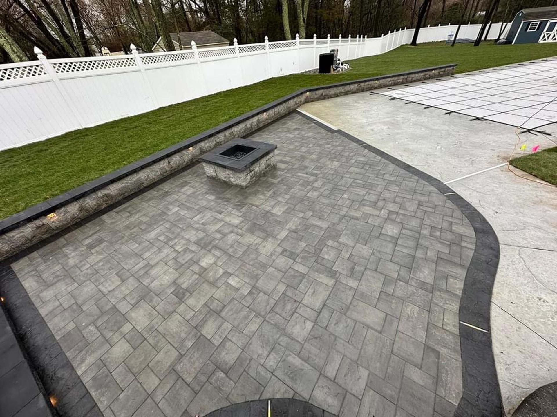 A patio with a fire pit and a white fence in the background.