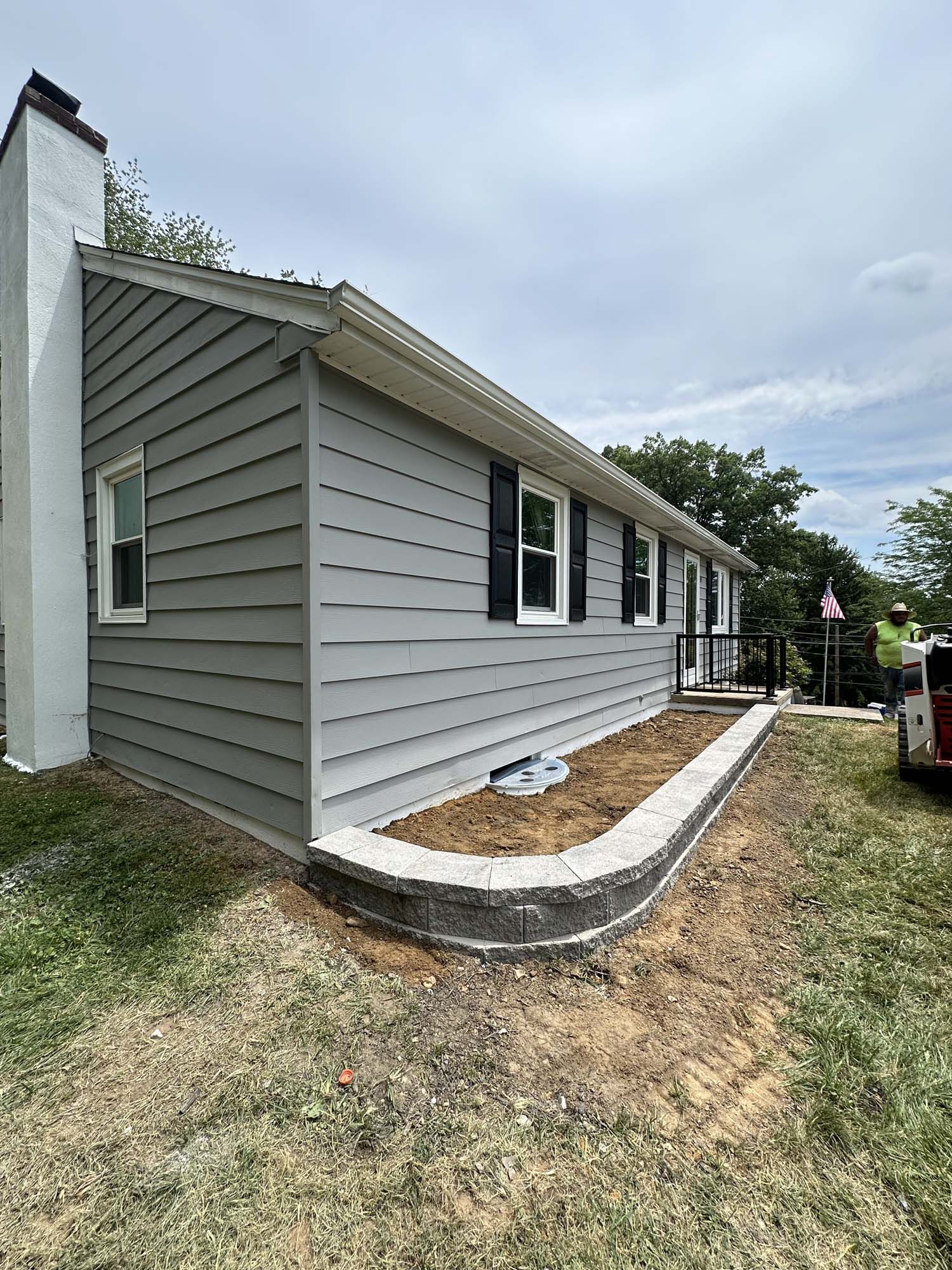 A house with a gray siding and black shutters is being remodeled.