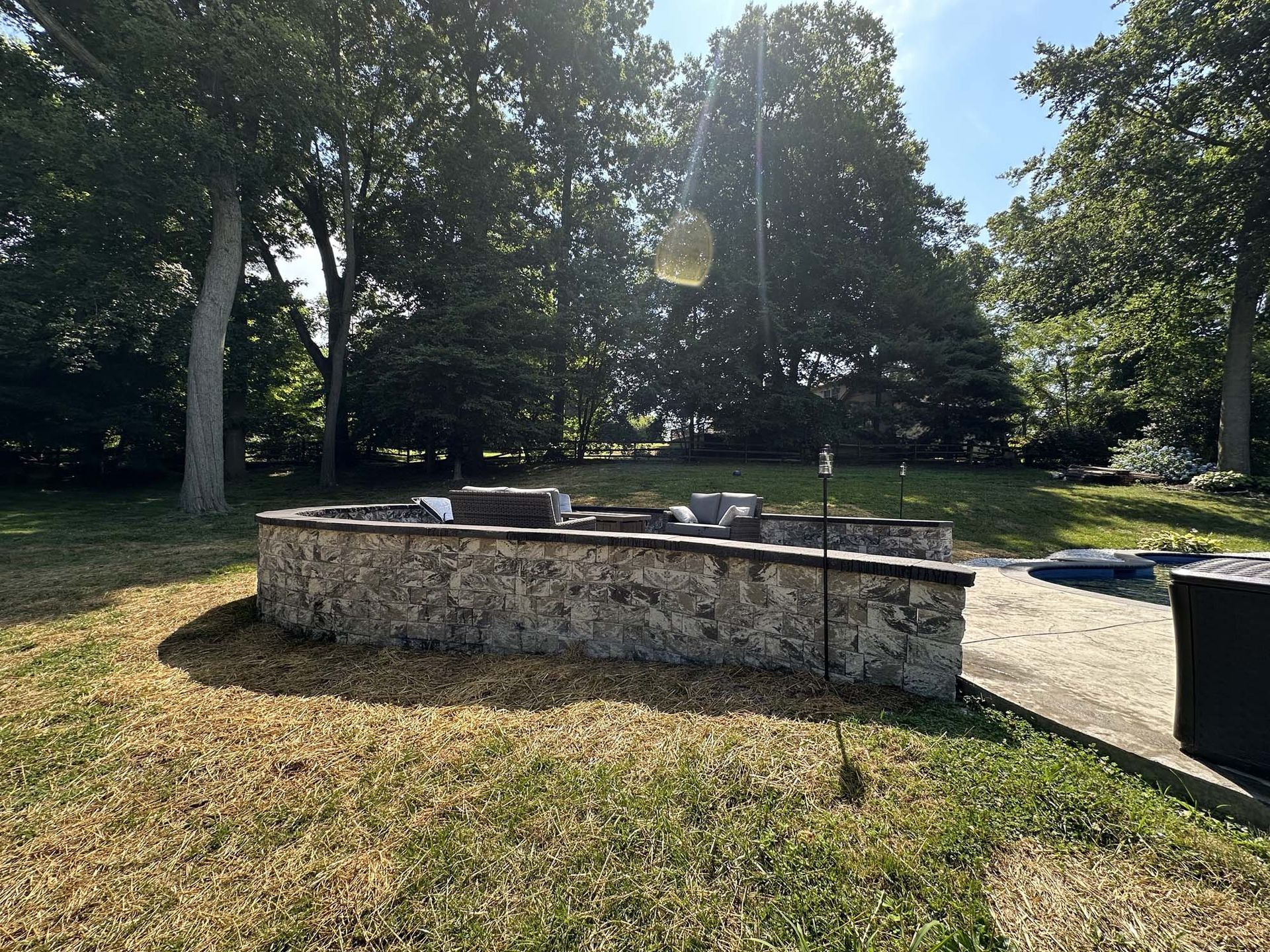A stone wall is in the middle of a lush green field surrounded by trees.