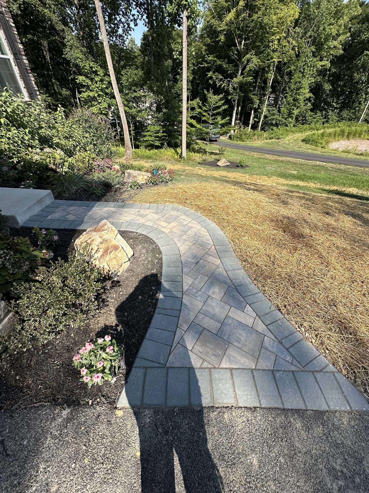 A brick walkway leading to a house with trees in the background.