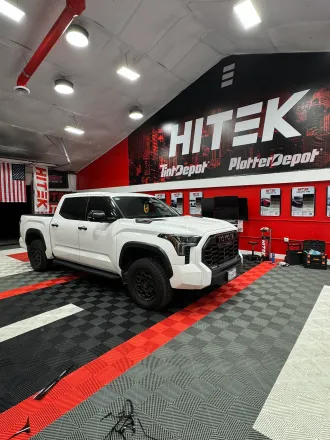White Toyota Tundra pickup truck inside a garage with black and red flooring and "Hitek" sign.