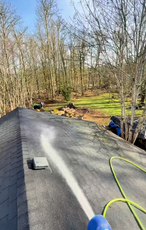 A person is cleaning the roof of a house with a high pressure washer.