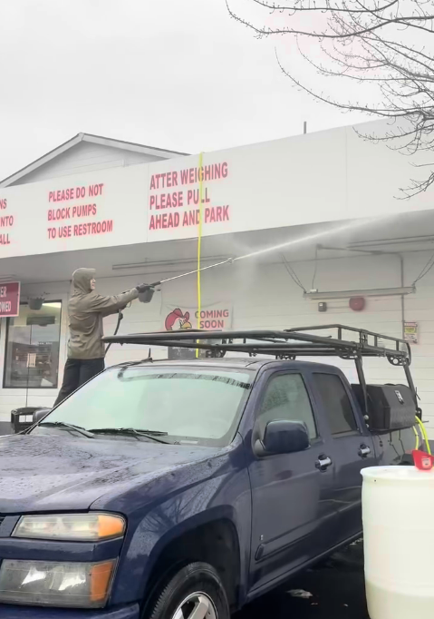 A man is washing a blue truck in front of a building.