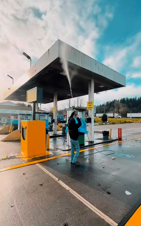 A man is cleaning a gas station with a high pressure washer.