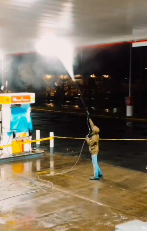 A man is using a high pressure washer to clean a gas station
