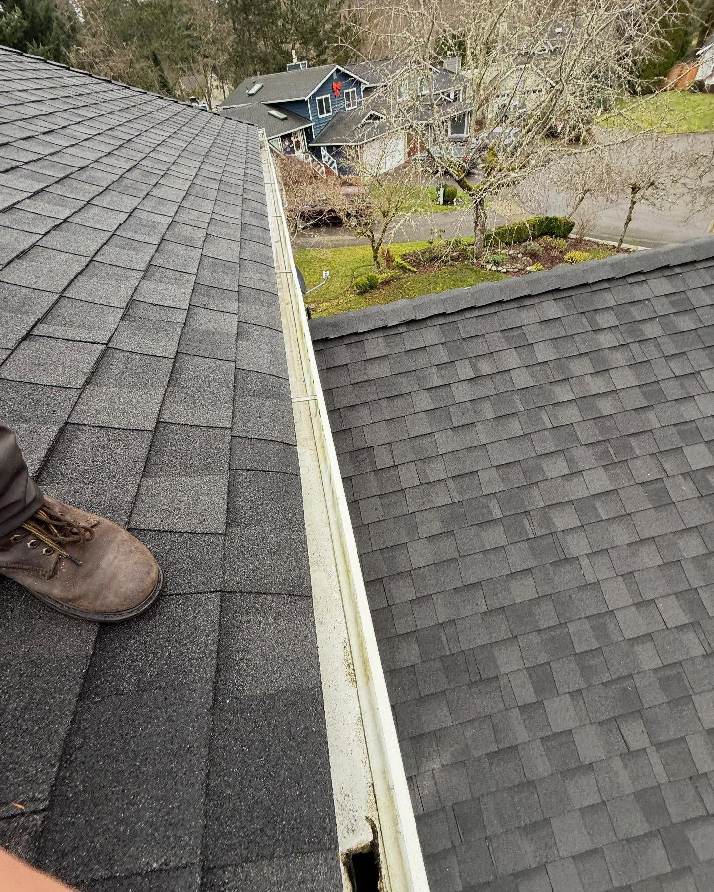 A person is standing on top of a roof next to a gutter.