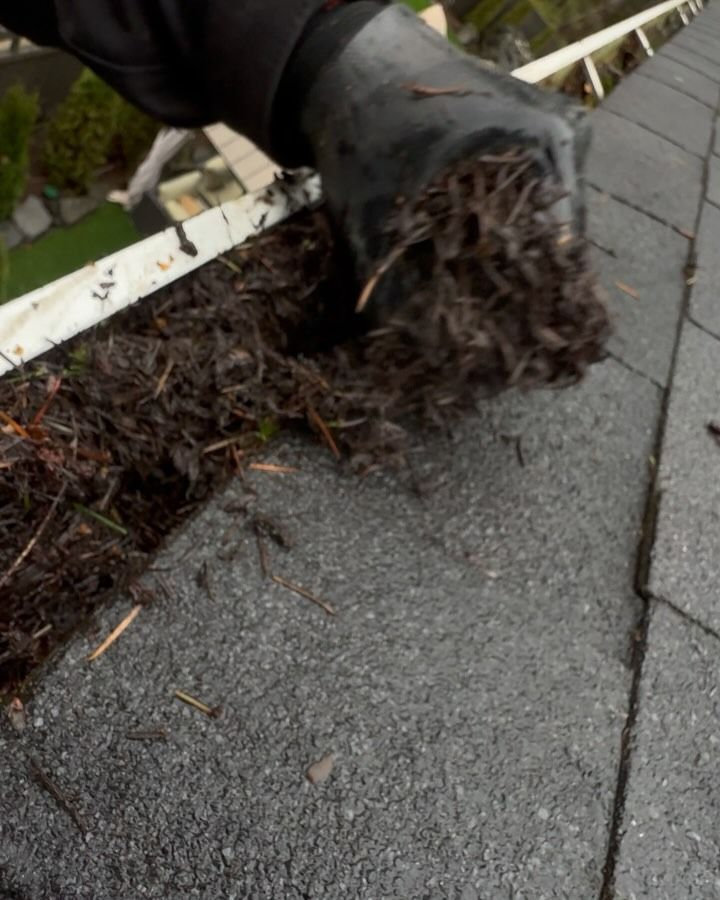 A person is cleaning a gutter on a roof with a broom.
