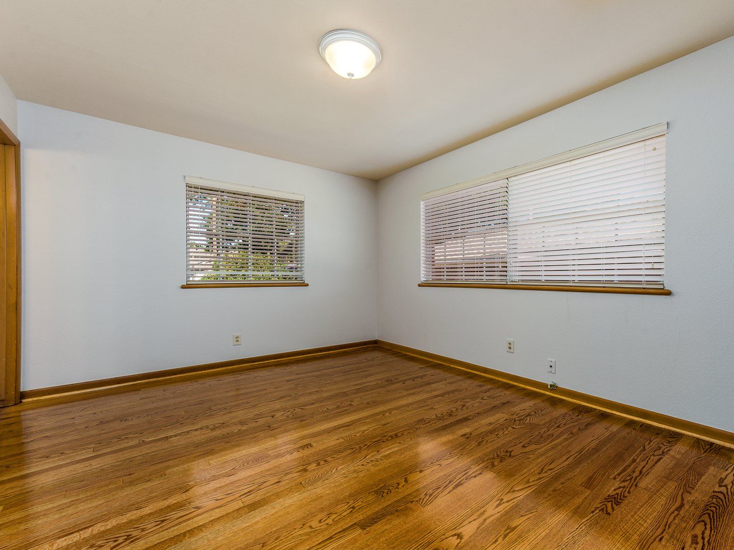 An empty room with hardwood floors and two windows