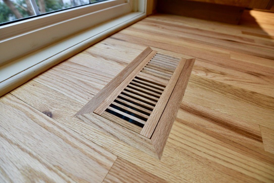 A wooden floor with a vent under a window