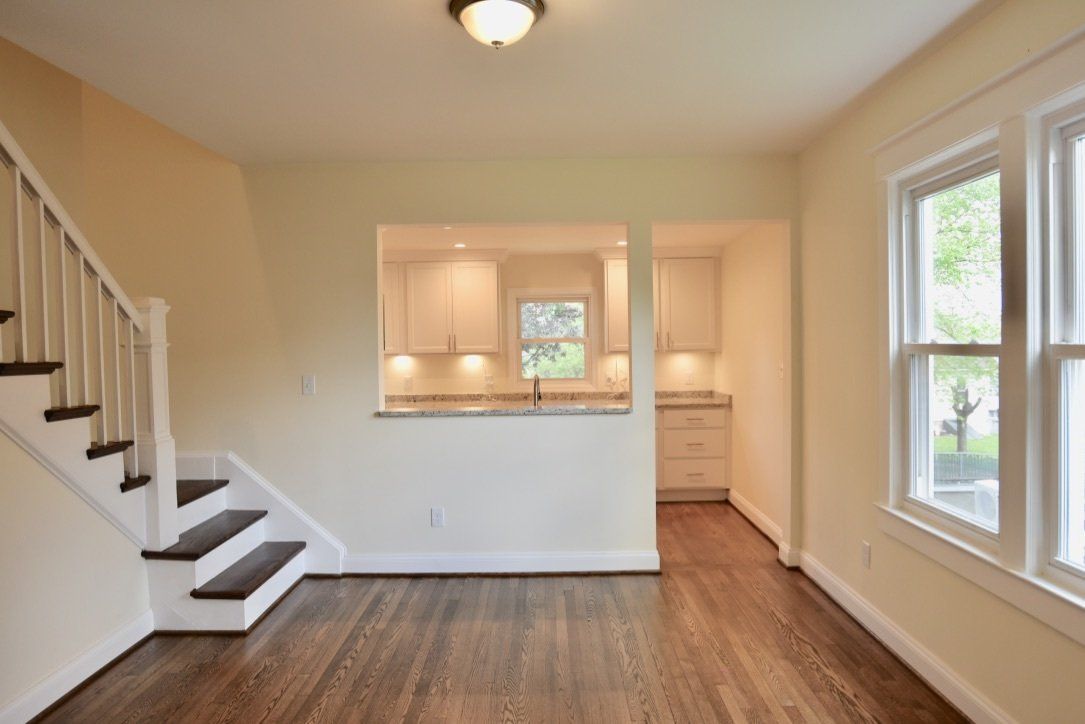 An empty living room with hardwood floors and stairs leading to the kitchen