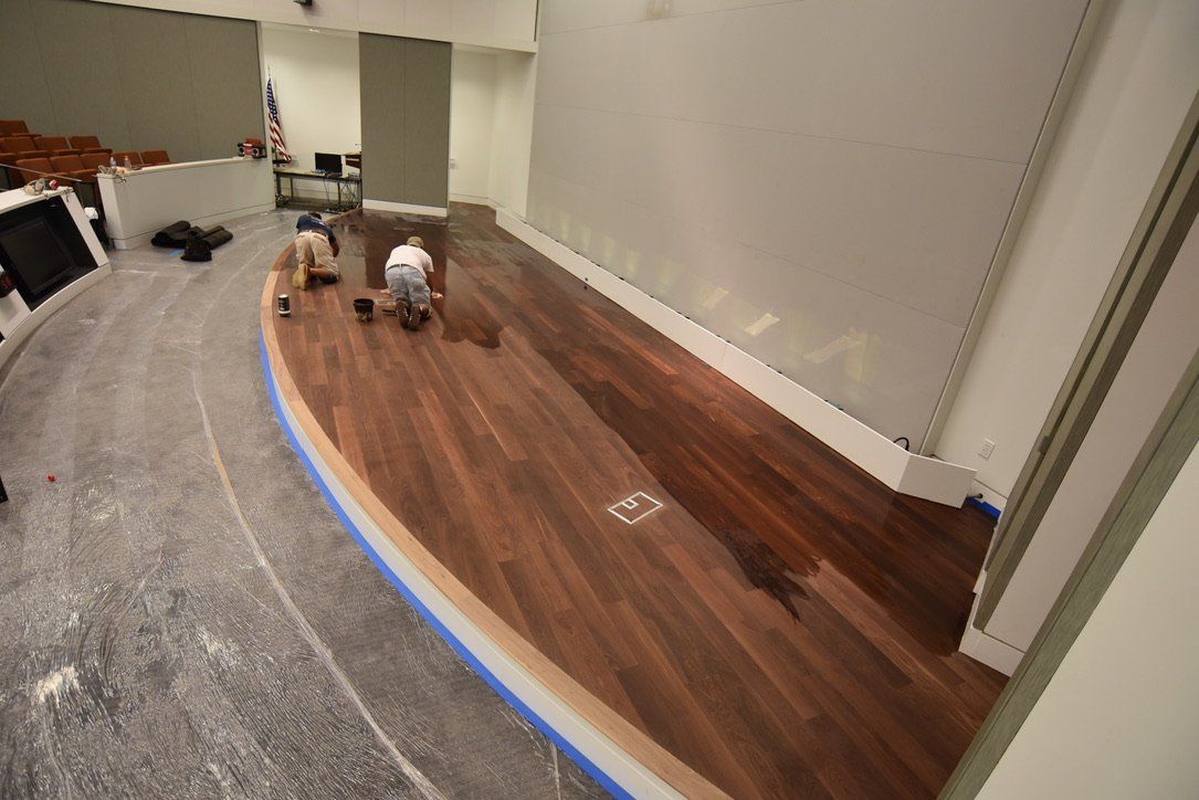 Two men are working on a wooden floor in an auditorium