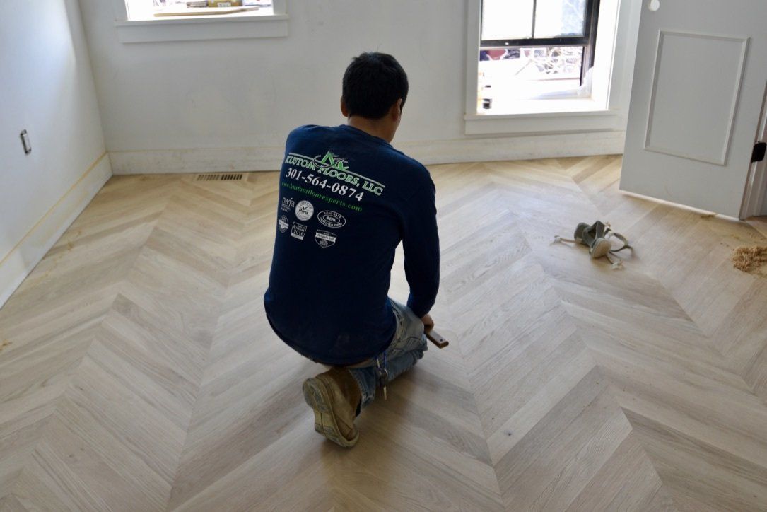 A man wearing a blue shirt with a green logo on the back is kneeling on a wooden floor