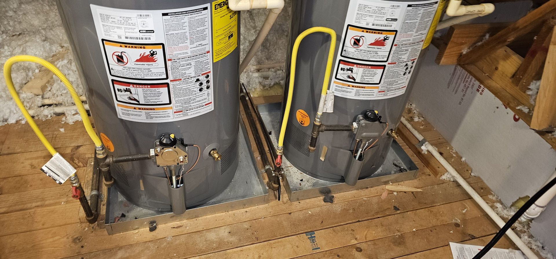 Two water heaters are sitting on top of a wooden floor.