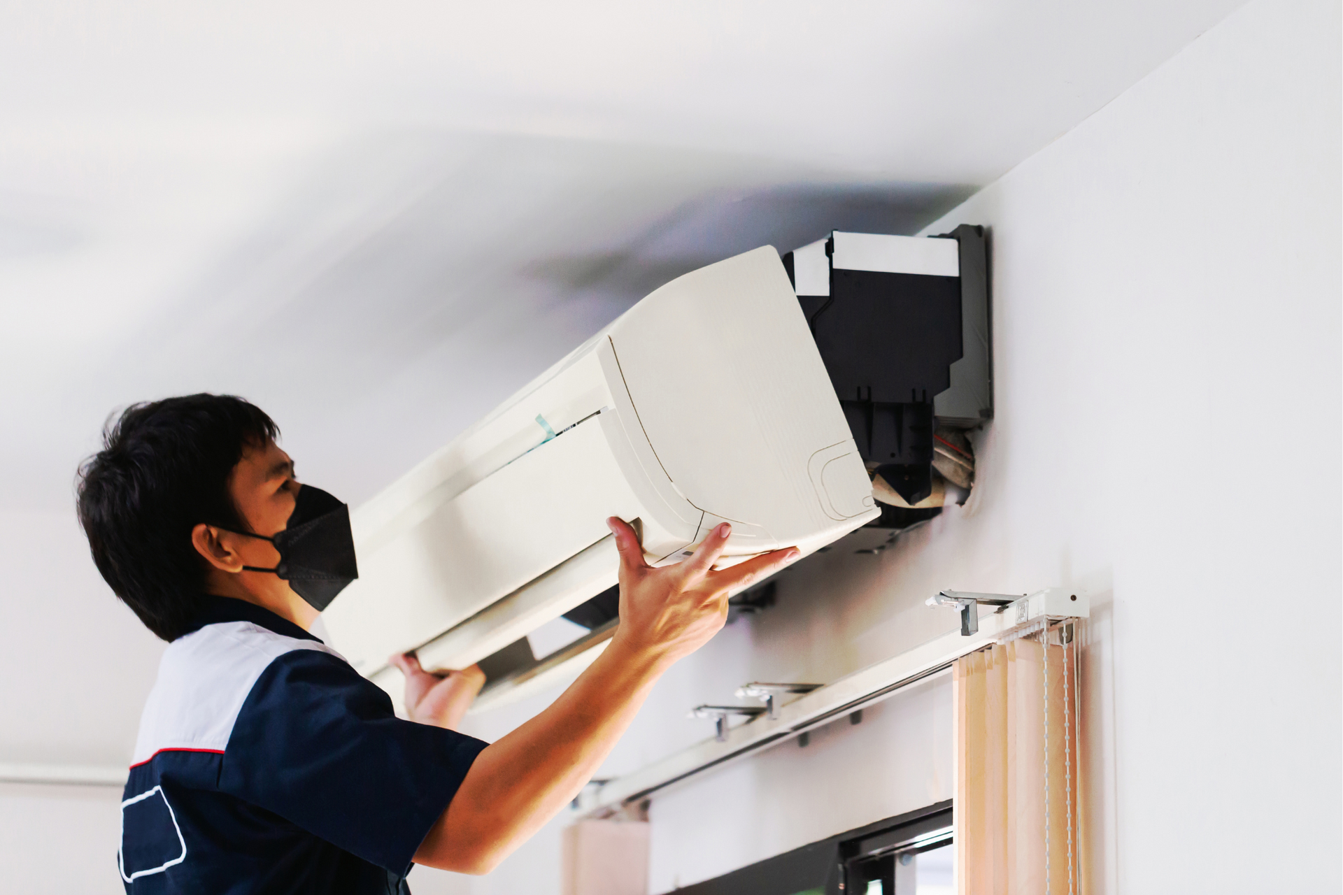 A man wearing a mask is fixing an air conditioner on the wall.