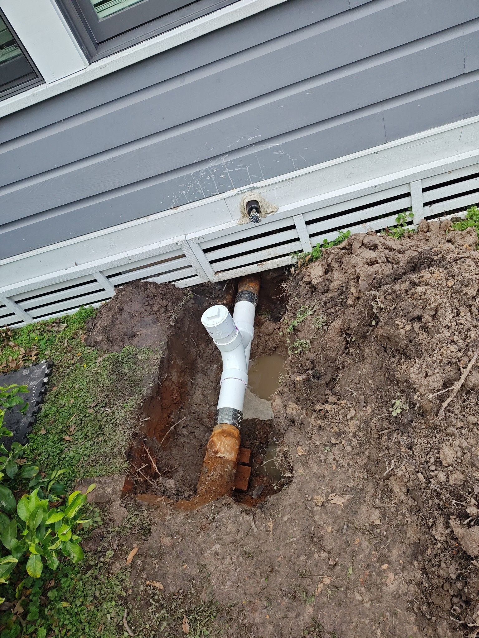 A drain pipe is being installed in the dirt next to a house.
