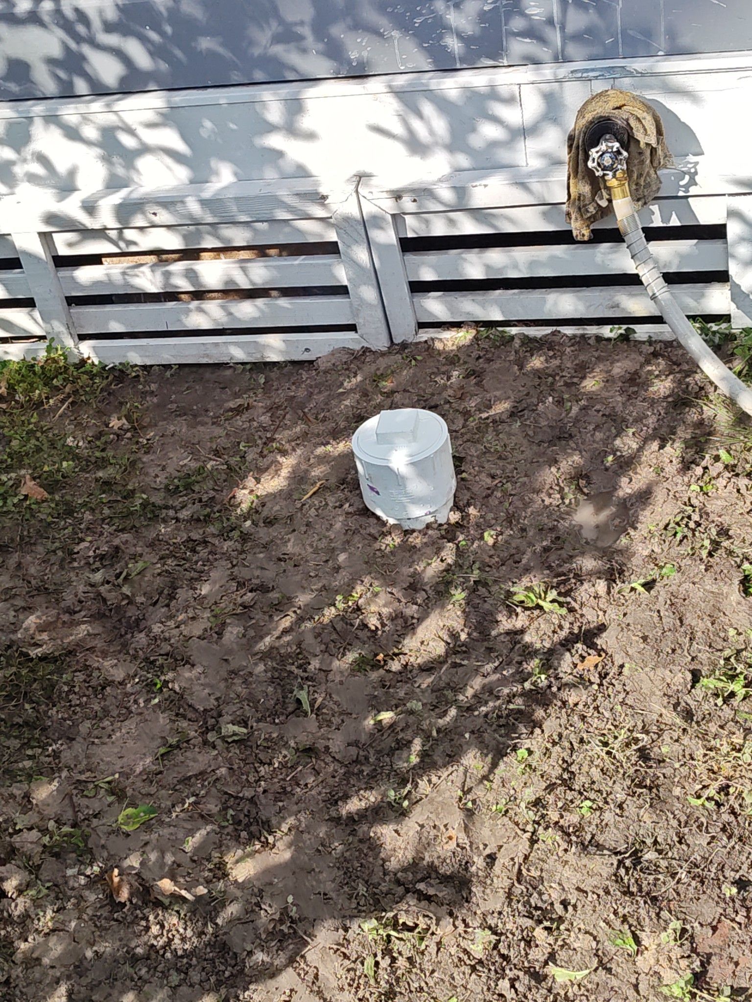A white bucket is sitting in the dirt next to a white fence.