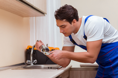 A plumber is fixing a faucet in a kitchen.