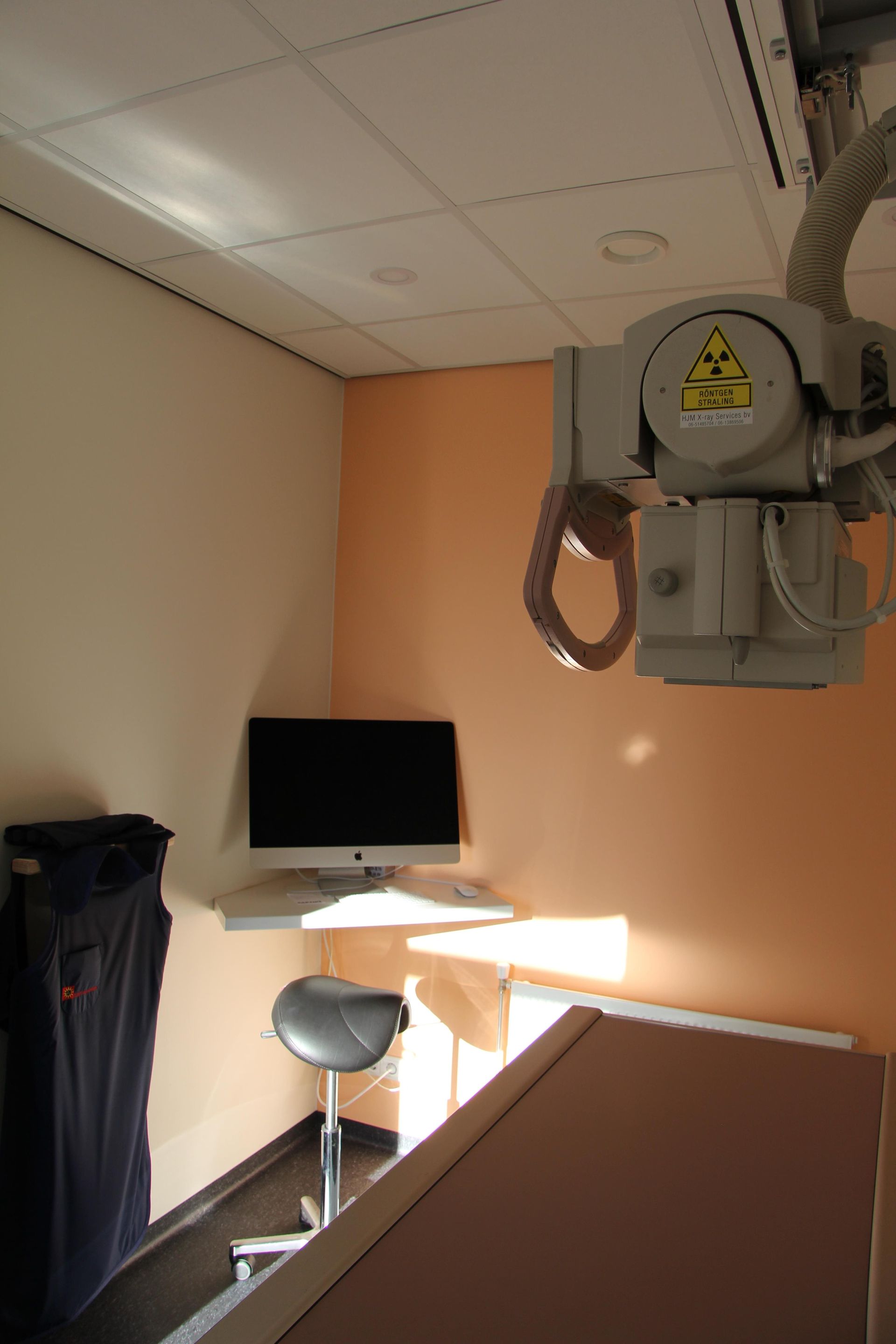 Kleine behandelkamer met een kruk, een aan de muur gemonteerde monitor en een tandheelkundig röntgenapparaat.