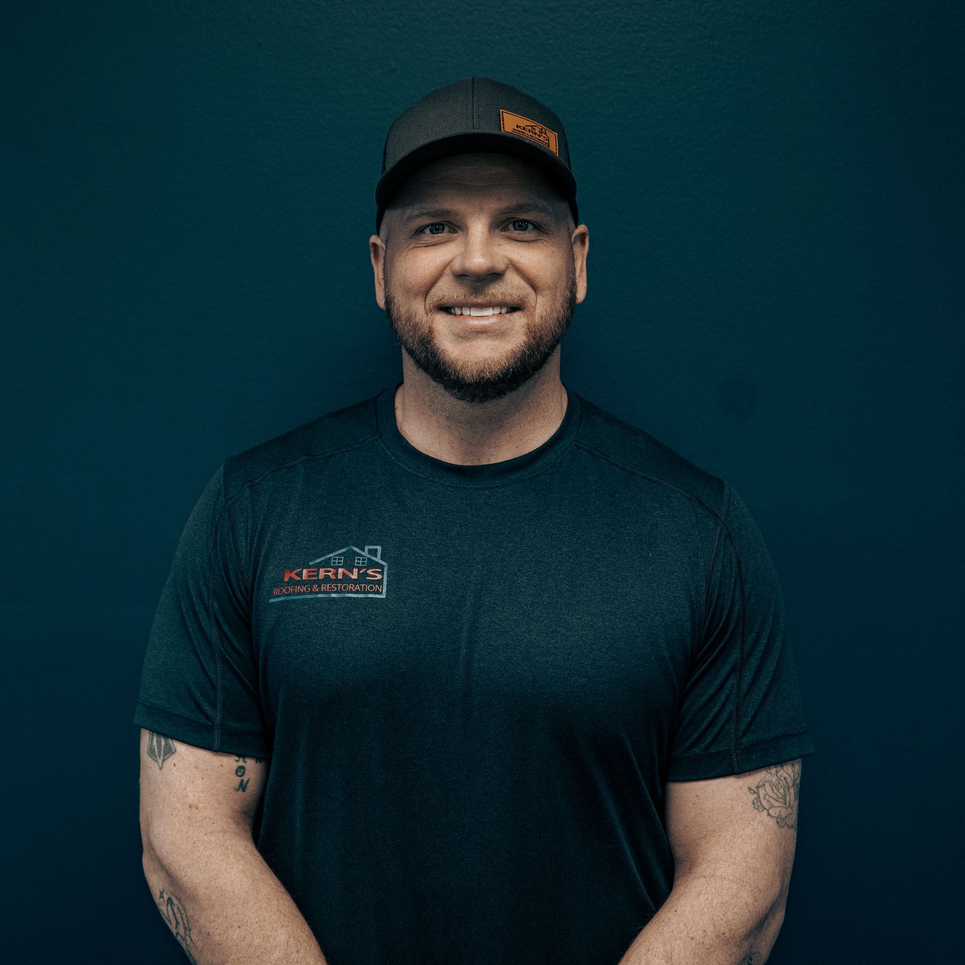Smiling man in a black cap and T-shirt against a teal background