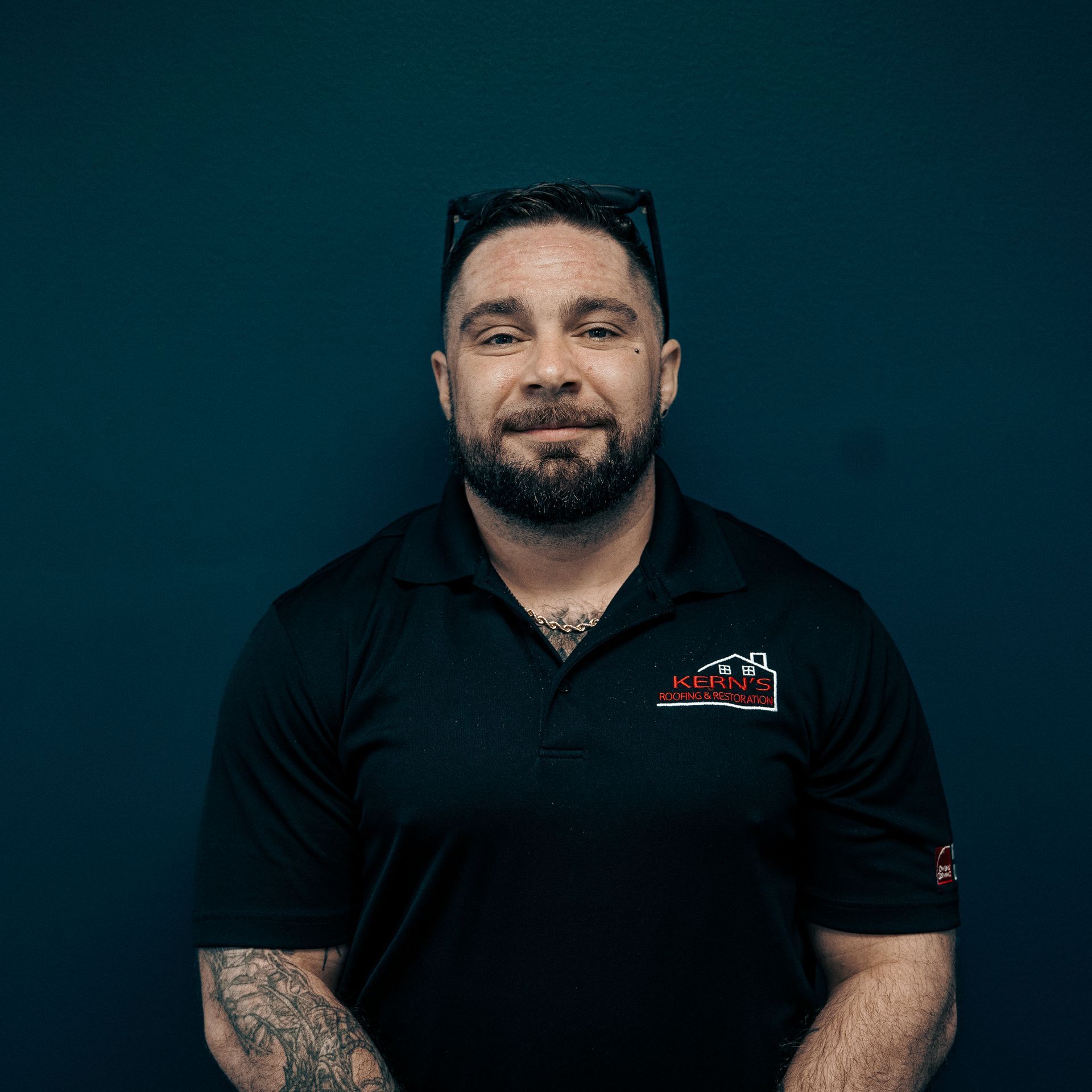 Portrait of a bearded man in a black polo shirt against a dark teal background