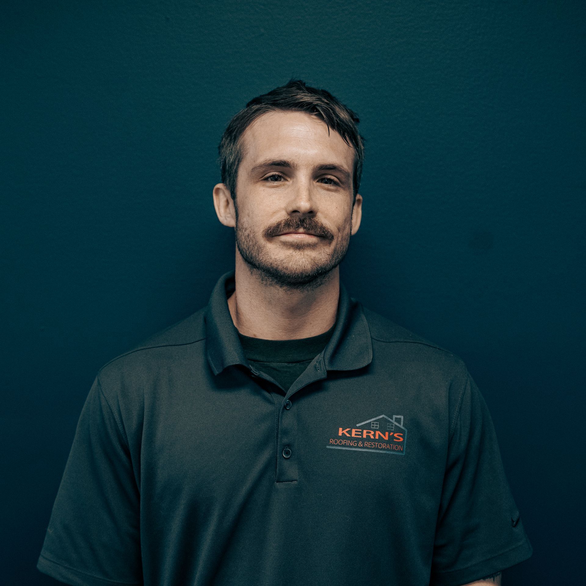 Portrait of a man in a dark green polo shirt against a teal background