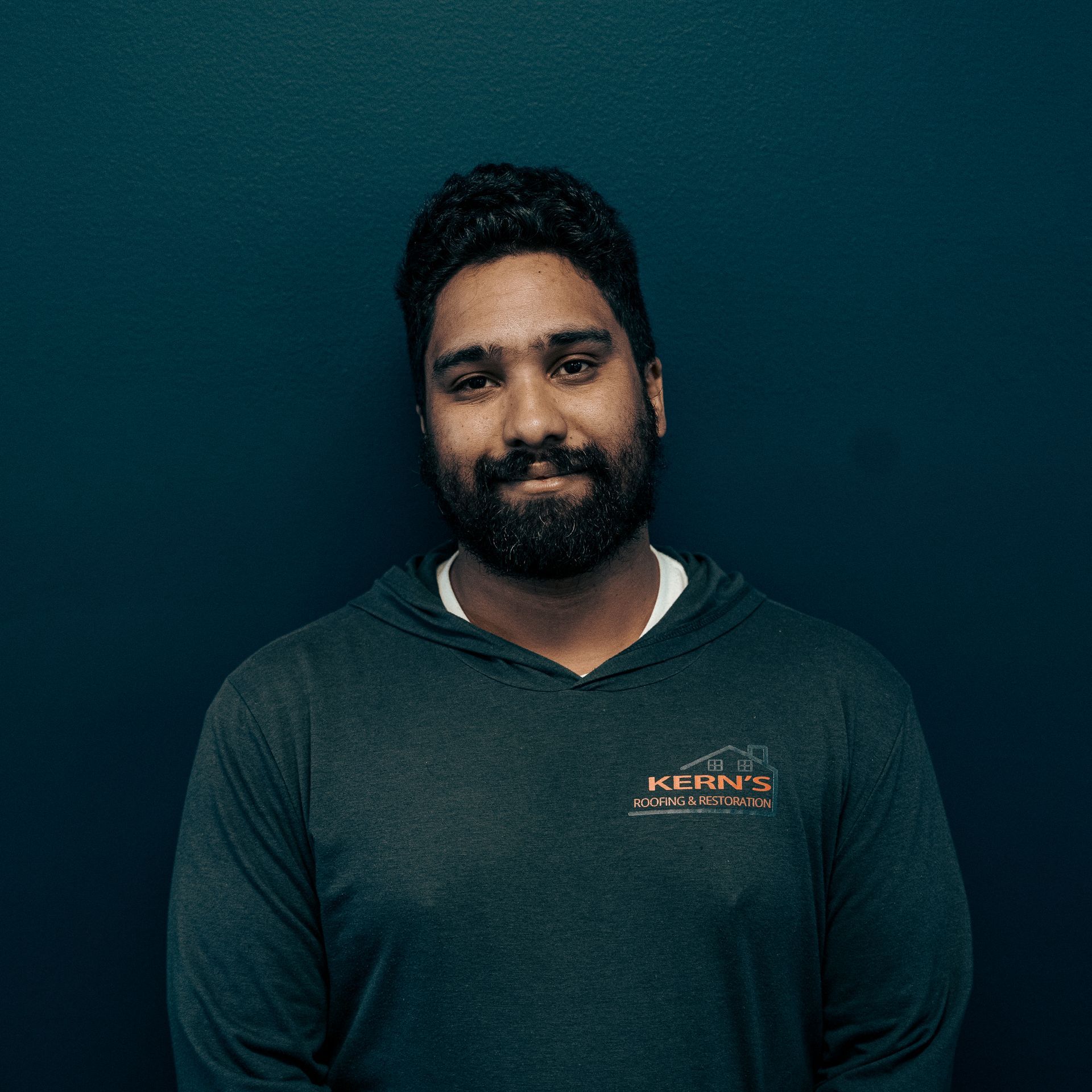 Portrait of a man with a beard in a dark shirt against a dark teal background