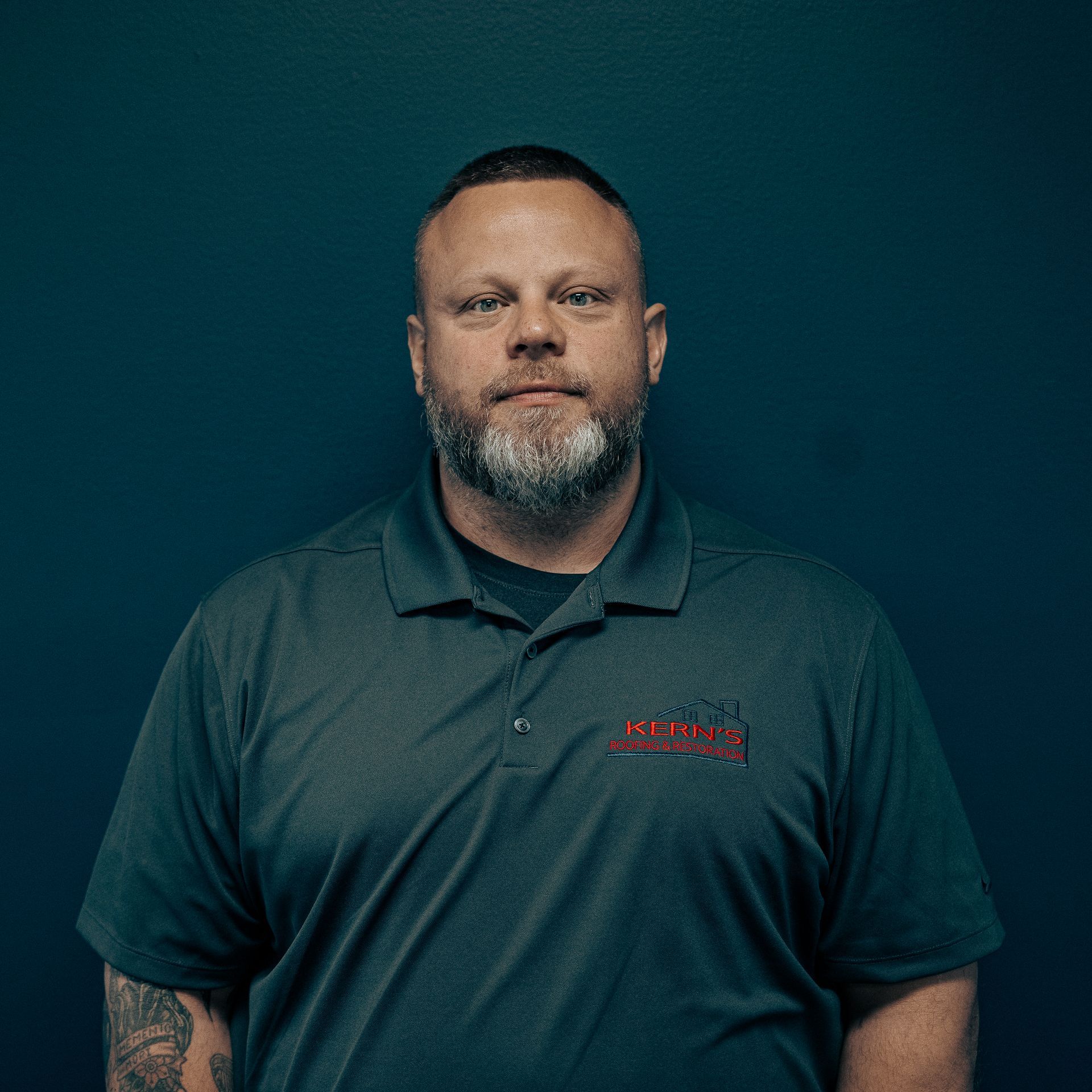 Portrait of a man in a dark polo shirt against a teal background
