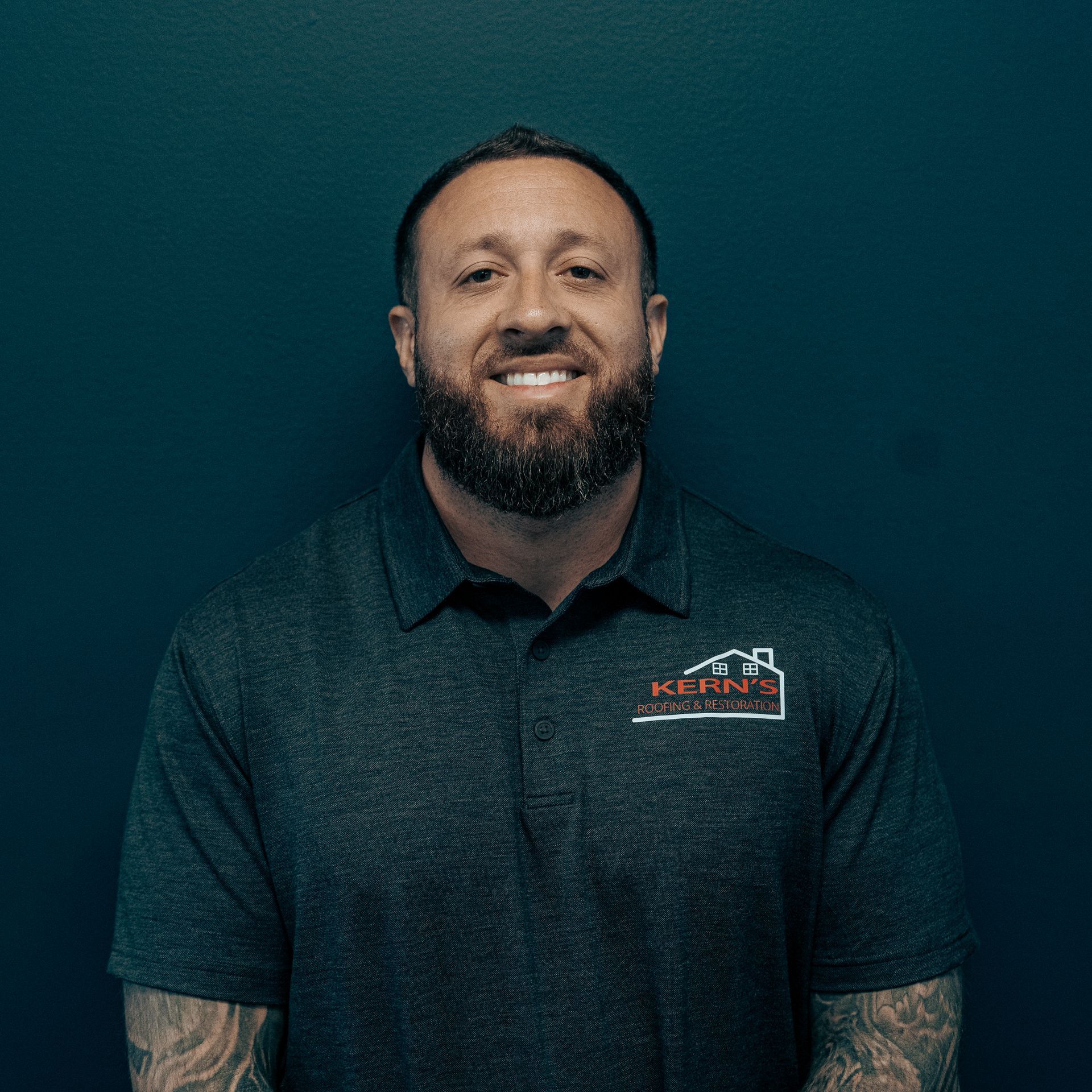 Smiling man in a dark polo shirt against a dark teal background