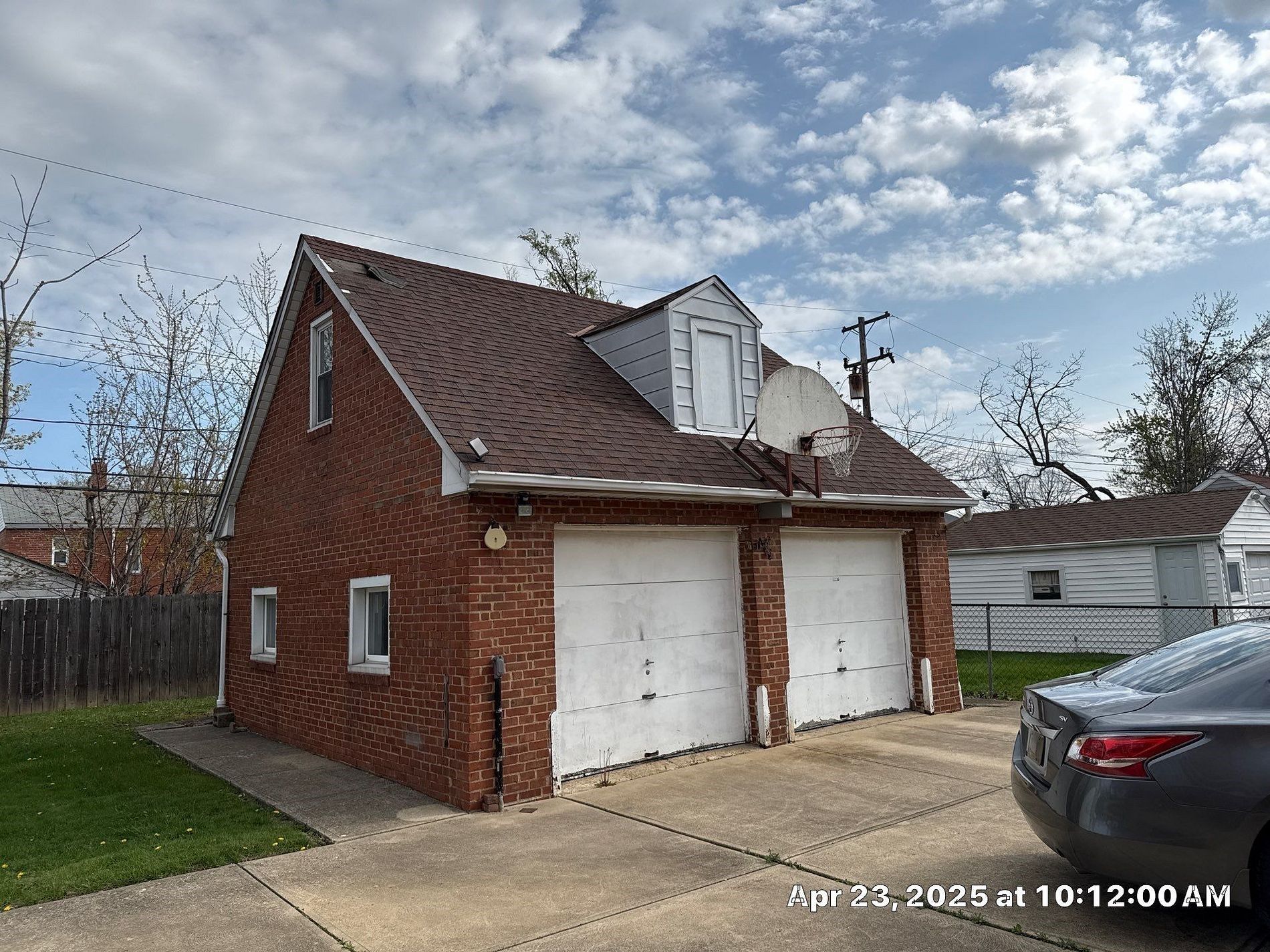 Two-car brick garage with white doors and a small white gable on the roof, under a cloudy sky. A car is parked in the driveway.