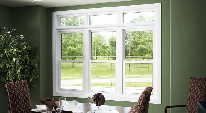 White framed window in a green-walled dining room overlooking a sunny, green landscape.