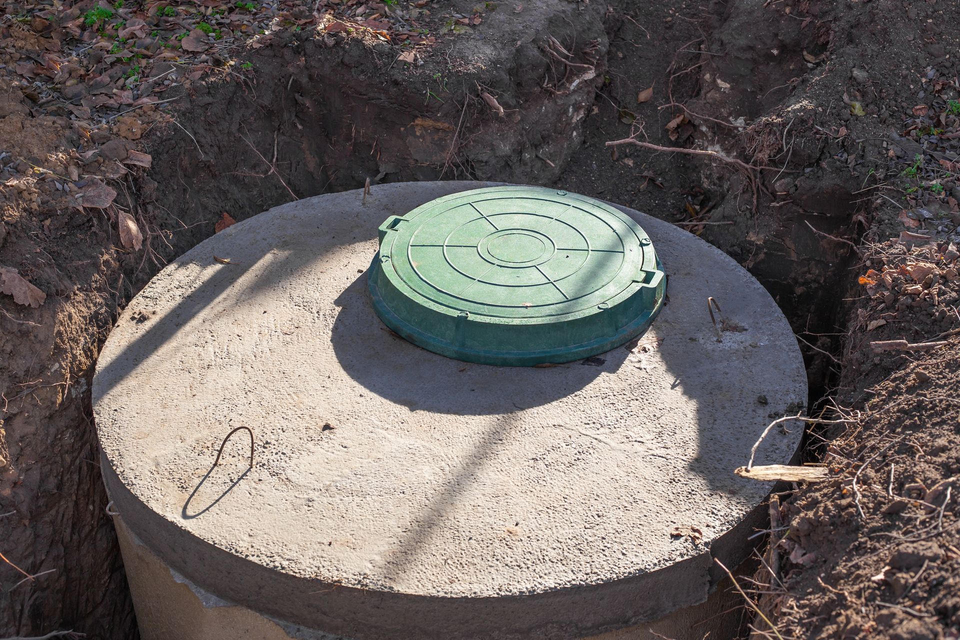 A concrete septic tank with a green lid is sitting in the dirt.
