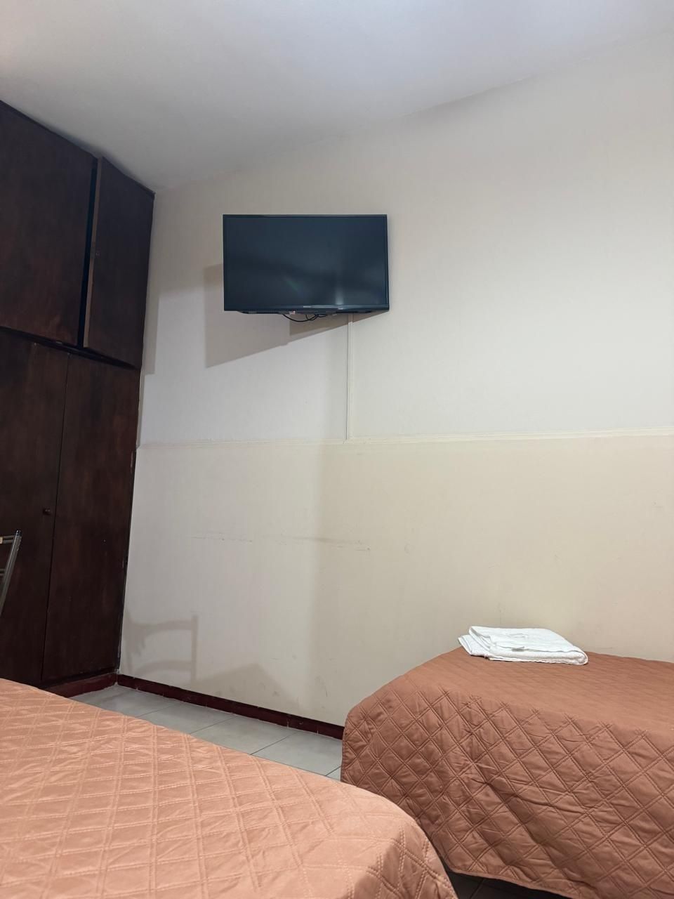 Una habitación de hotel con dos camas con colchas acolchadas de color marrón, un armario de madera