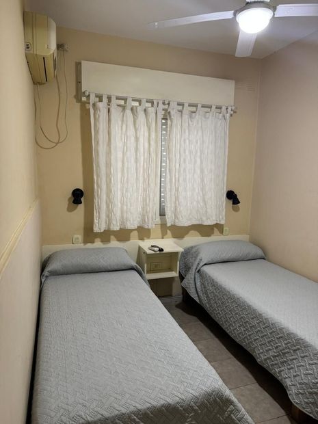 Dos camas individuales con colchas grises estampadas en una habitación con una mesita de noche central