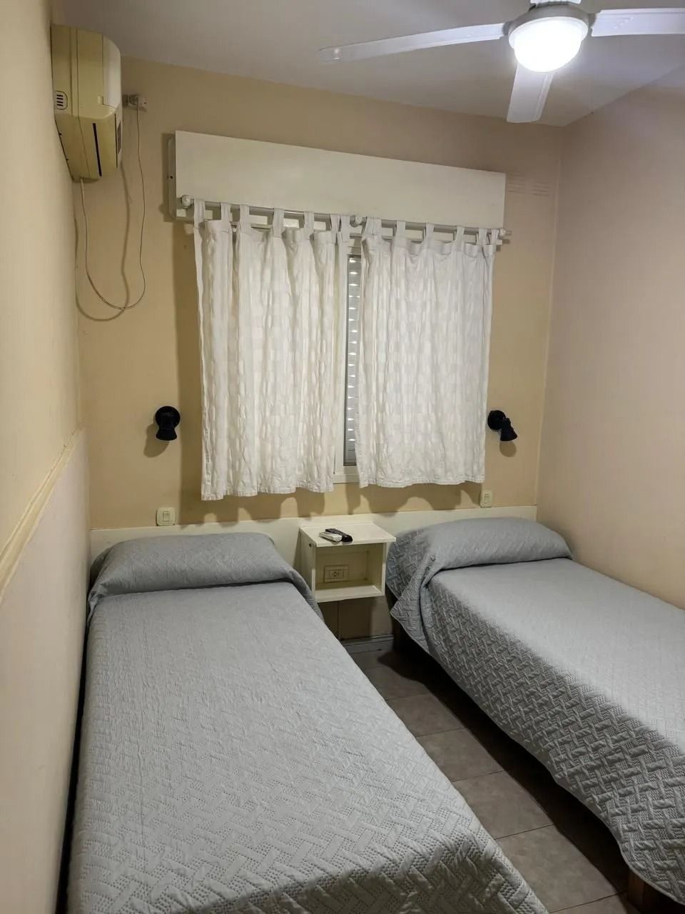 Dos camas individuales con colchas grises estampadas en un dormitorio con paredes beige