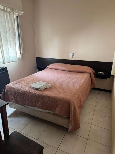 Una habitación de hotel con una cama tamaño queen, una colcha color salmón, un cabecero de madera