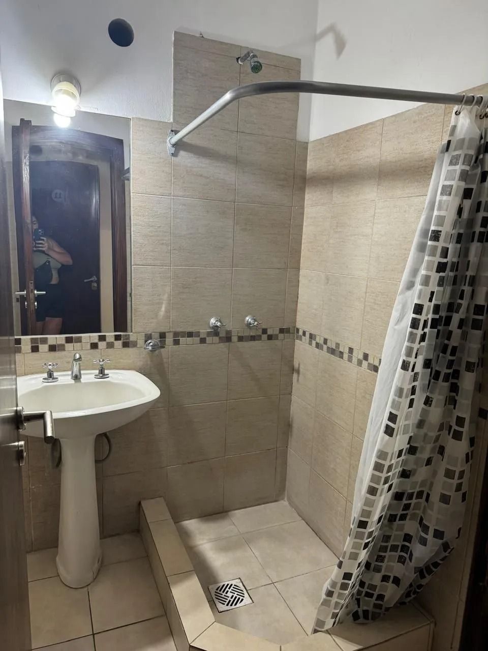 En un baño pequeño, un lavabo con pedestal se encuentra junto a una ducha a ras de suelo con una cortina