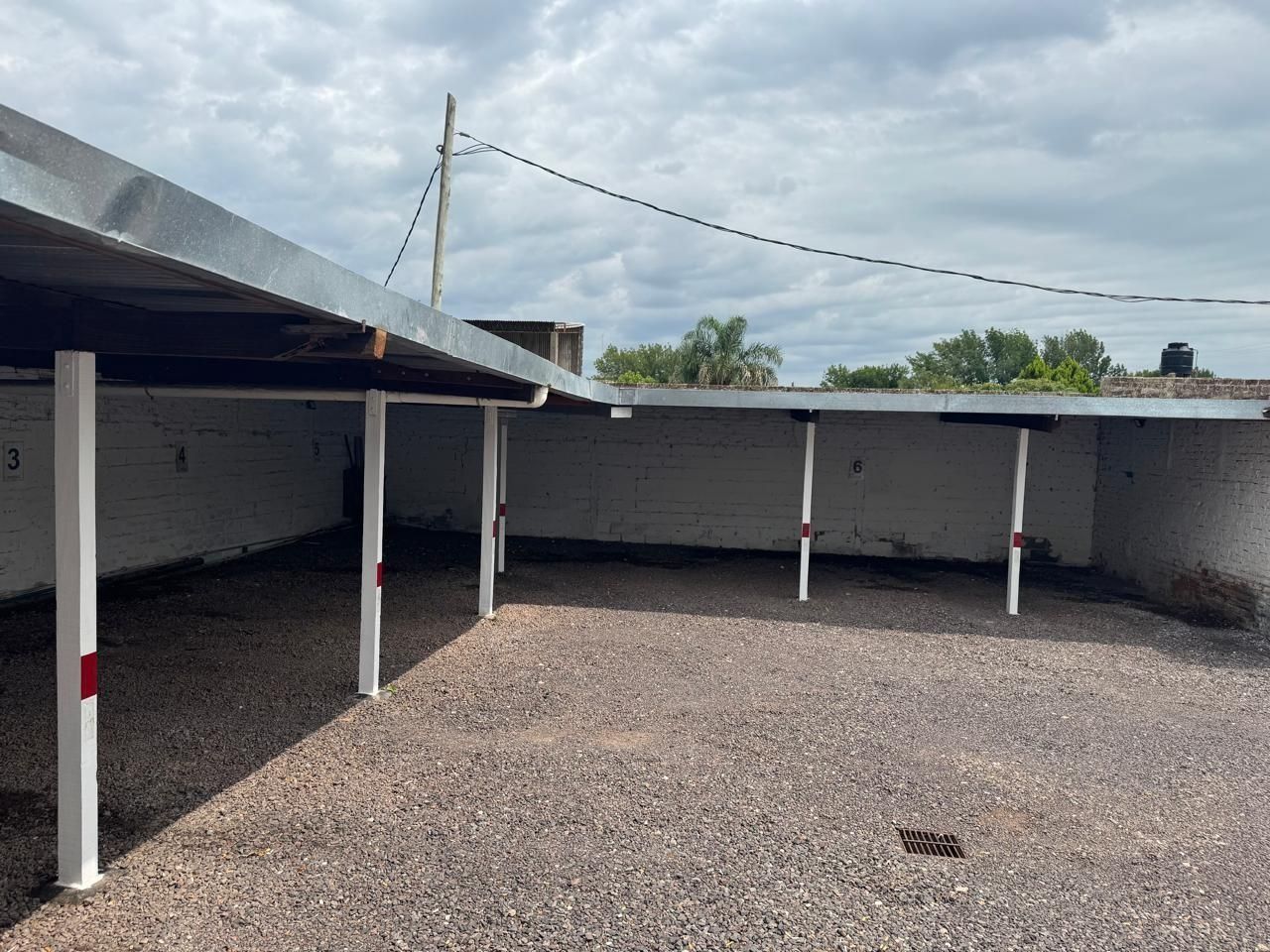 Un aparcamiento al aire libre con techo metálico sostenido por pilares blancos sobre un suelo de grava