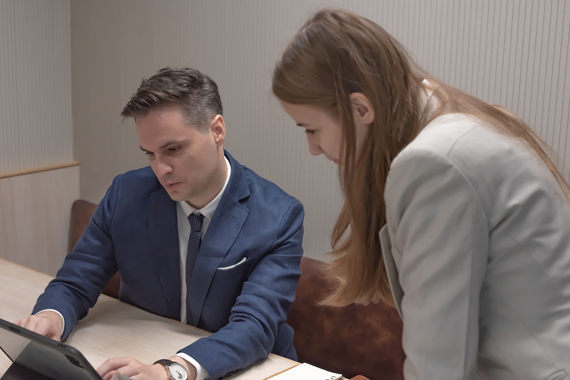 Man and woman in business attire looking at a tablet in an office setting.